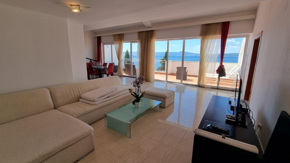 Svetlý obývací priestor s krémovým gaučom a modernou dlažbou. Skvelý výhľad na more.