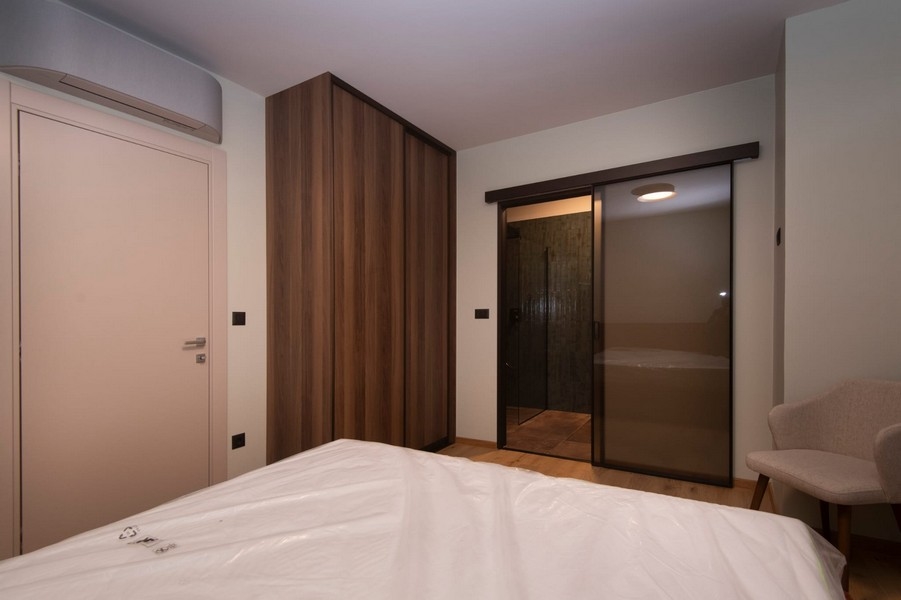 Spálňa s priamym prístupom do kúpeľne v modernom apartmáne na predaj v Splite v Chorvátsku s veľkou posteľou a elegantným nábytkom.