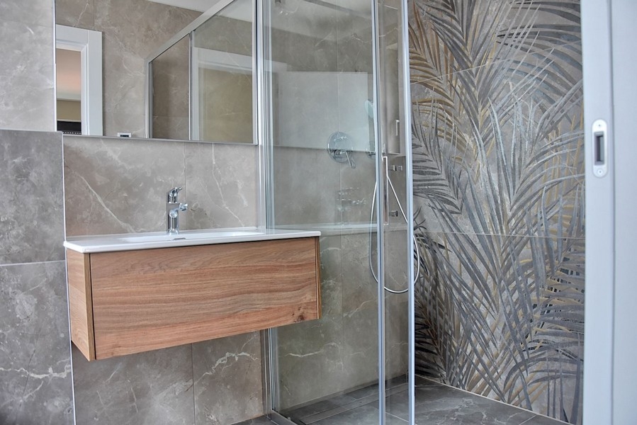 Moderná kúpeľňa v strešnom apartmáne na Istrii so sprchovacím kútom s dekoratívnymi sklenenými obkladmi a dreveným umývadlom.