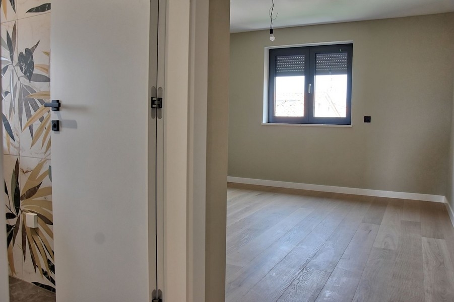 Spálňa v strešnom apartmáne na predaj na Istrii s veľkými dekoratívnymi obkladmi a drevenými podlahami.