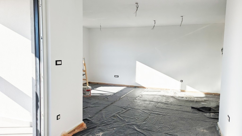 Priestranná, slnkom presvetlená izba s ochrannou fóliou na podlahe, v priebehu dokončovania prvotriedneho bytu na Istrii