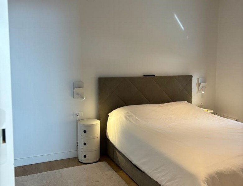 Minimalistická spálňa s veľkou posteľou a nočným stolíkom, súčasť nehnuteľnosti v Rijeke v Chorvátsku.