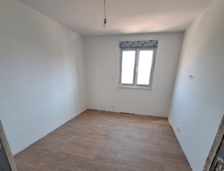 Prázdna miestnosť v plášti nového bytu s drevenými podlahami a oknom, biele steny, pripojenie stropného svetla, nehnuteľnosť Panorama Skauting v Chorvátsku.