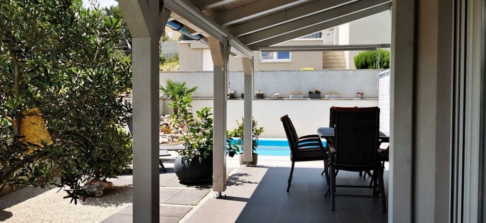 Krytá terasa s vonkajším jedálenským kútom, časť bytu na predaj v Tisne, Chorvátsko, s výhľadom na bazén.