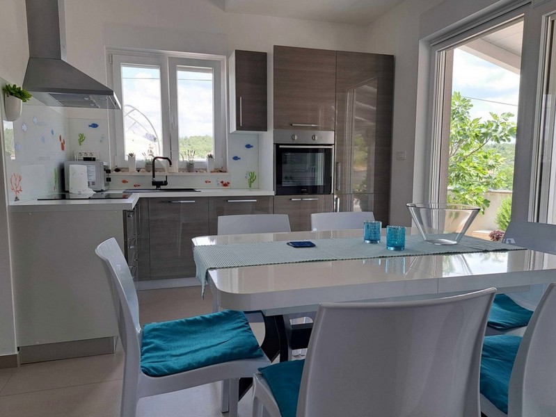 Moderná kuchyňa s bielym nábytkom a jedálenským kútom v byte na predaj v Tisne, Chorvátsko.