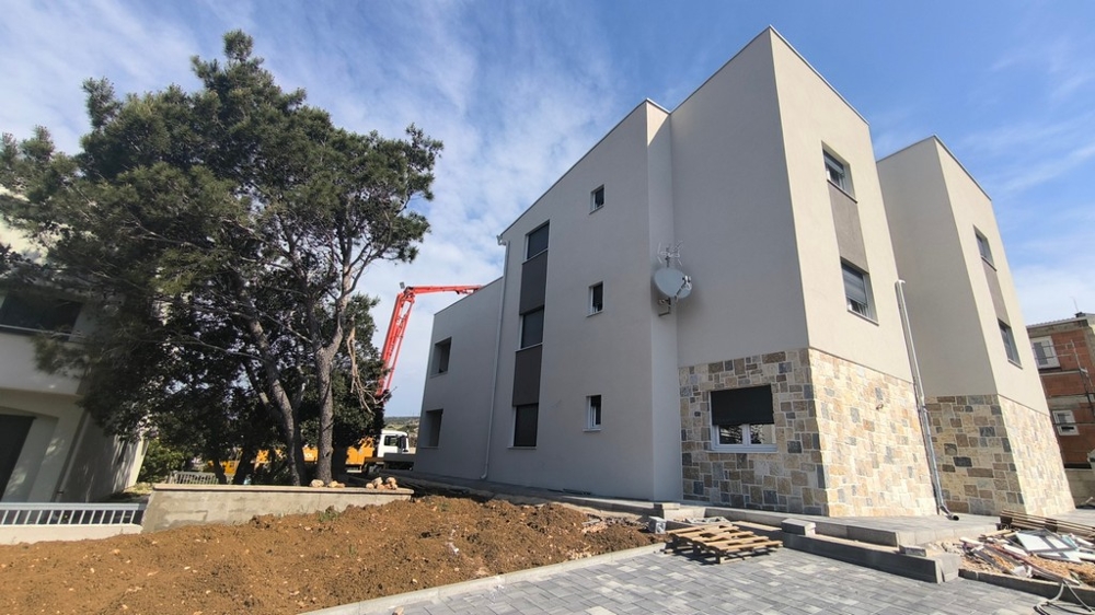 Novostavba moderného strešného bytu v Chorvátsku v Šimuni s vonkajšími parkovacími miestami a stromom v popredí.