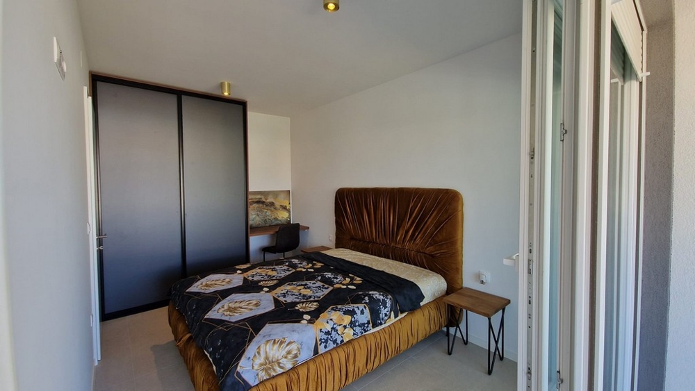 Spálňa apartmánu v Novalji, ostrov Pag, s hnedou posteľou a prístupom na balkón, nehnuteľnosť Chorvátsko