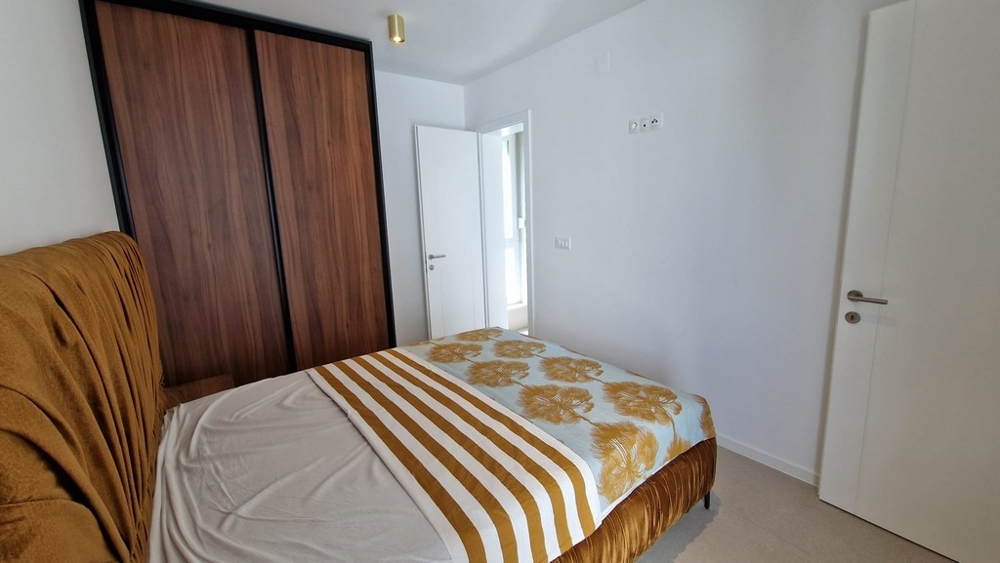 Spálňa apartmánu v Novalji, ostrov Pag, s pruhovanou posteľnou bielizňou a drevenými prvkami, chorvátska nehnuteľnosť