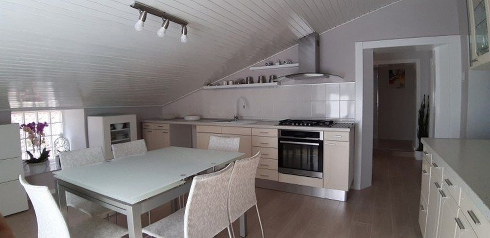 Moderná svetlá kuchyňa s bielym interiérom a jedálenským kútom pod šikmým stropom