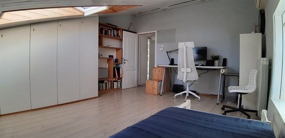 Pracovňa s písacím stolom, policami a jednolôžkom, všetko vo svetlej miestnosti so strešným oknom