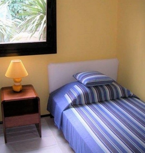 Malá spálňa so žltými stenami, jednolôžkom a nočným stolíkom s lampou