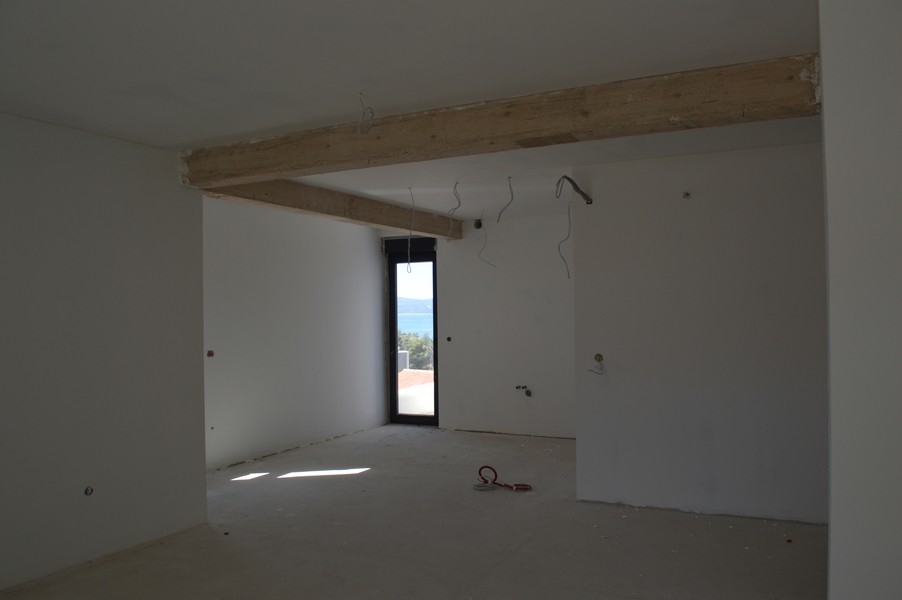 Priestranná obývacia izba v nedokončenom apartmáne s odhalenými trámami a výhľadom na more.