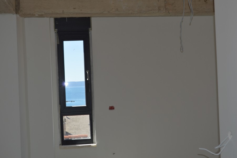 Úzke okno v nedokončenom byte s výhľadom na more.