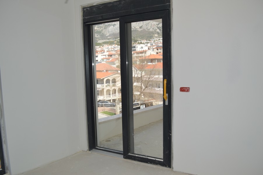 Balkónové dvere v rozostavanom byte s výhľadom na okolité domy a hory.