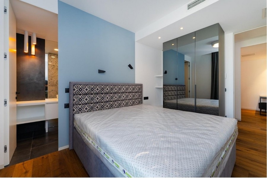 Spálňa s modro-bielymi stenami, sivá posteľ, zrkadlová skrinka