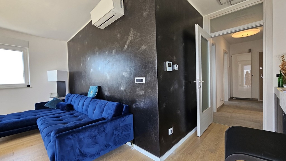 Obývacia izba s modrým gaučom, klimatizáciou a čiernou stenou