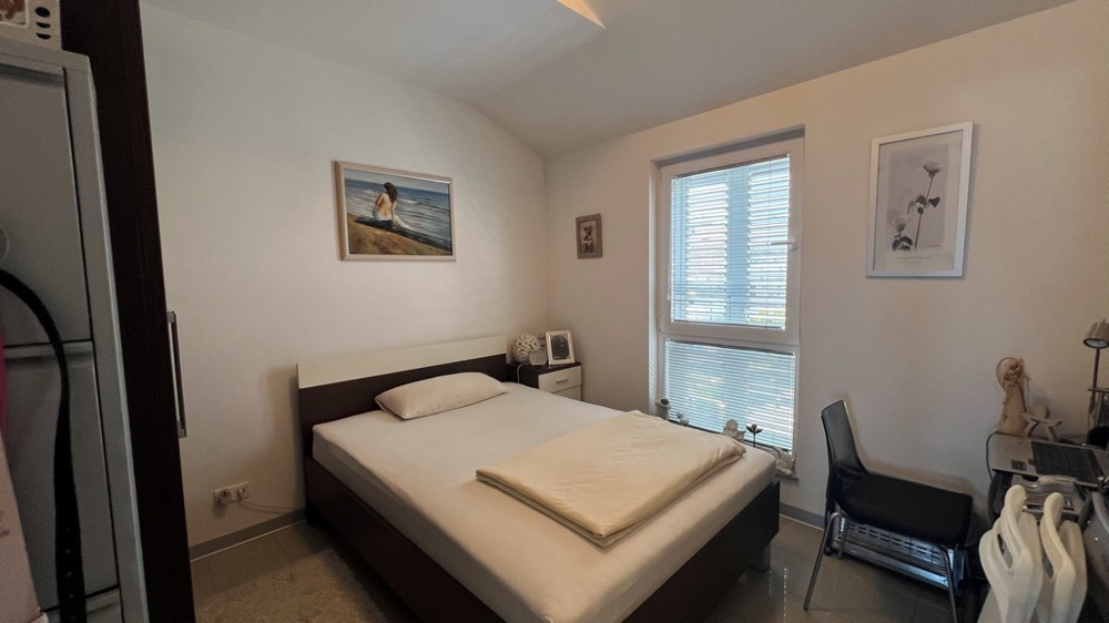 Spálňa s manželskou posteľou, jednoducho zariadená s oknom do záhrady.