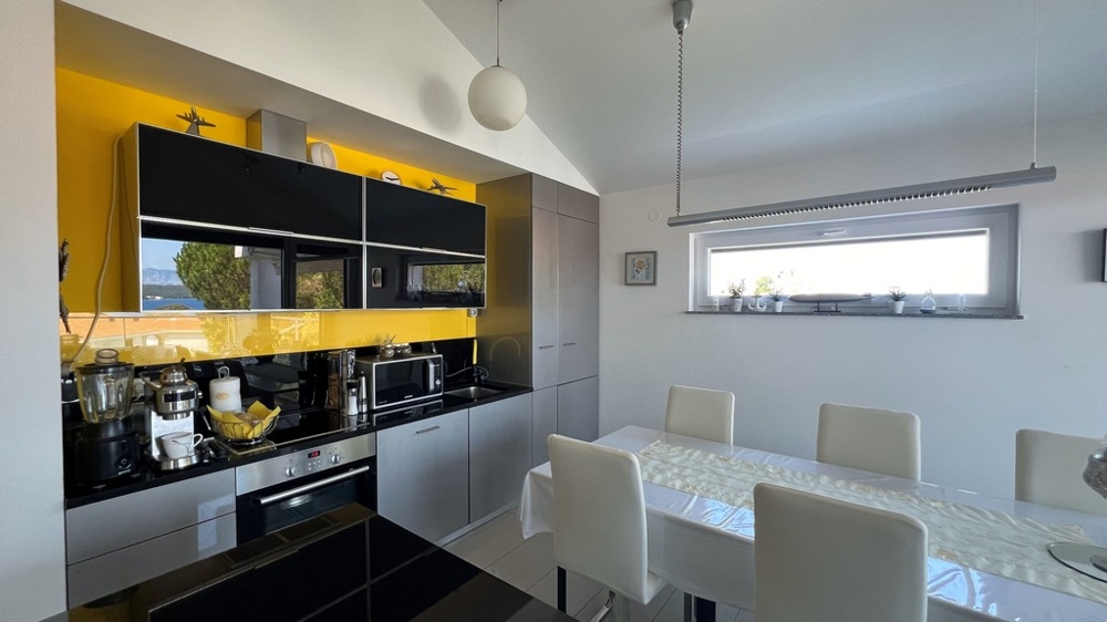 Moderná kuchyňa s čiernou pracovnou doskou a žltou zadnou stenou, priľahlý jedálenský kút.