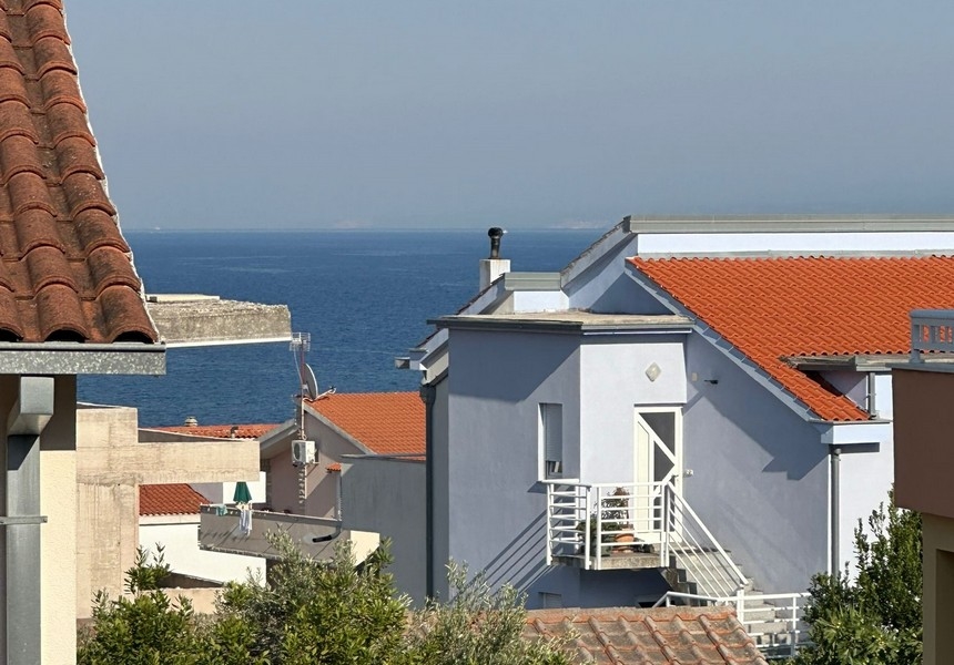 Pohľad na obytnú štvrť s domom s červenou škridlovou strechou s výhľadom na modré more a vzdialené pobrežie