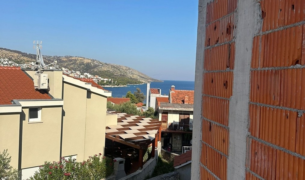 Čiastočne dokončená budova s ​​odhalenými tehlami s výhľadom na štvrť s červenými škridlovými strechami a na more v pozadí