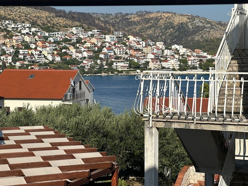 Malebný výhľad na pobrežné mesto s domami s červenými strechami, zelenou vegetáciou a kopcami v pozadí cez záliv