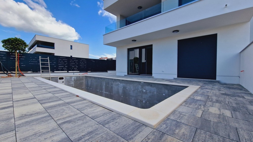 Bazén vo výstavbe pred modernou budovou so sklenenými balkónmi a veľkými terasami