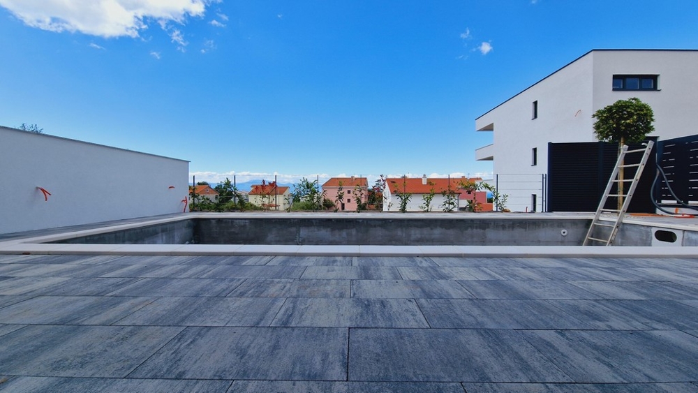 Nedokončený bazén vo vonkajšom areáli moderného obytného domu obklopeného spevneným terénom