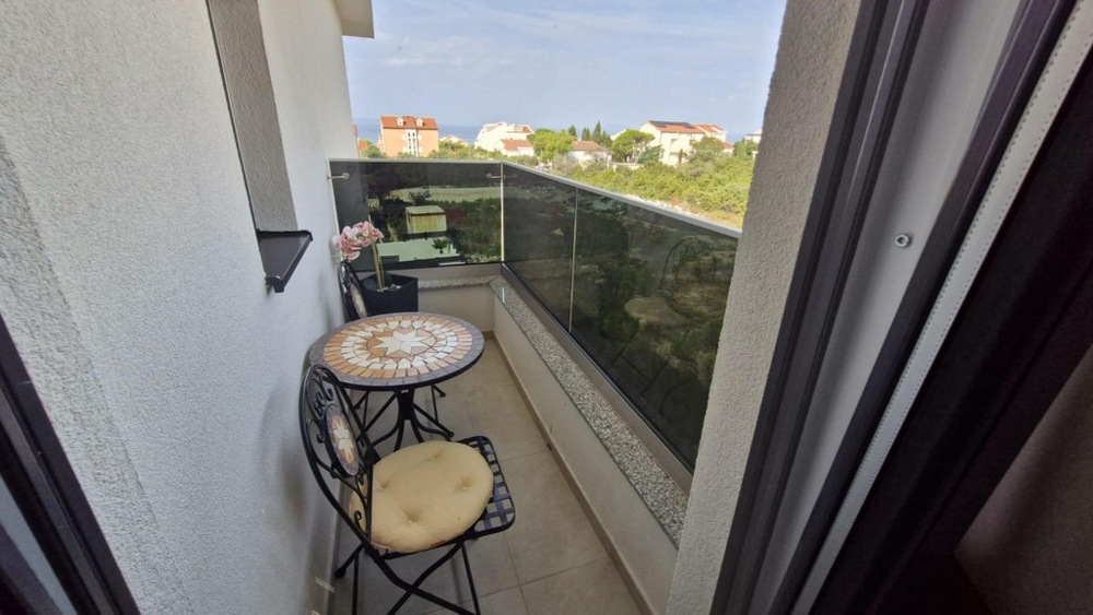 Balkón s malým stolíkom a dvoma stoličkami, výhľad na susedné budovy