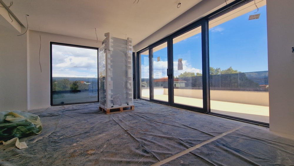 Vnútorný pohľad na moderný nový apartmán s veľkými oknami a výhľadom na terasu a more.