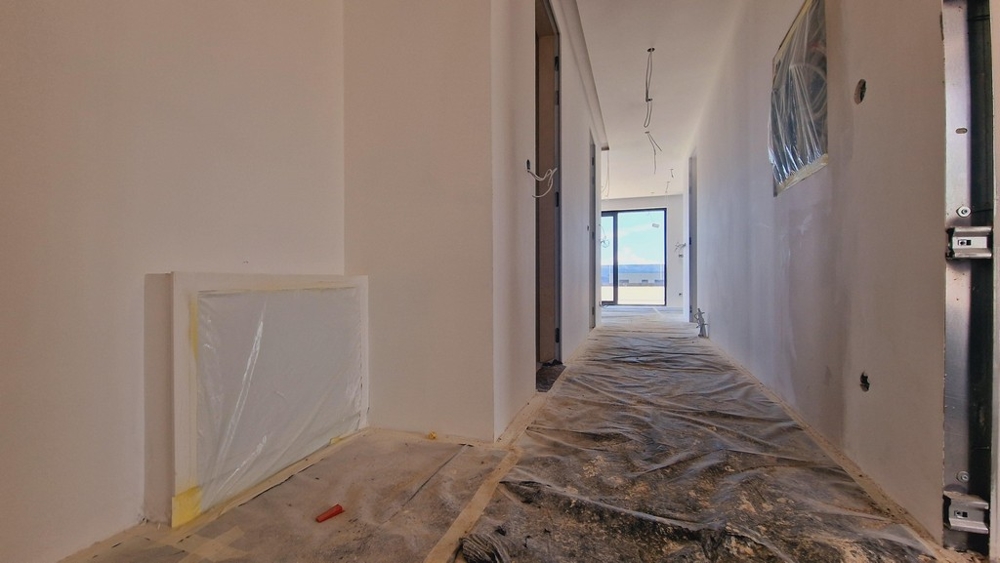 Predsieň novostavby vo fáze výstavby s výhľadom na terasu na konci chodby.