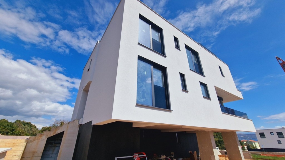 Vonkajší pohľad na modernú novostavbu s čistou, bielou fasádou a niekoľkými veľkými oknami.