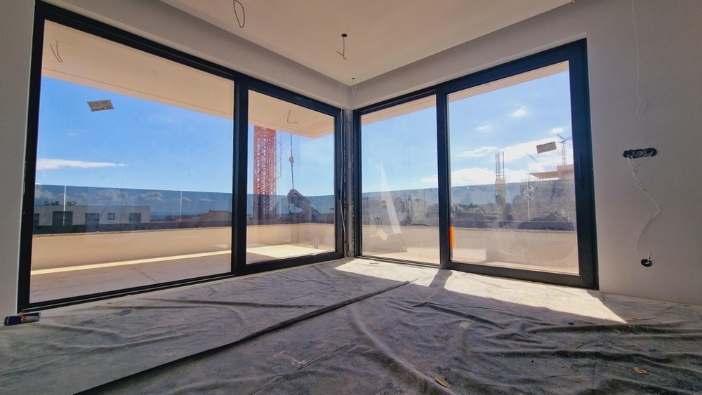 Obývacia izba s dvoma veľkými presklenými priečeliami, ktoré prepúšťajú množstvo prirodzeného svetla a ponúkajú výhľad na okolie.