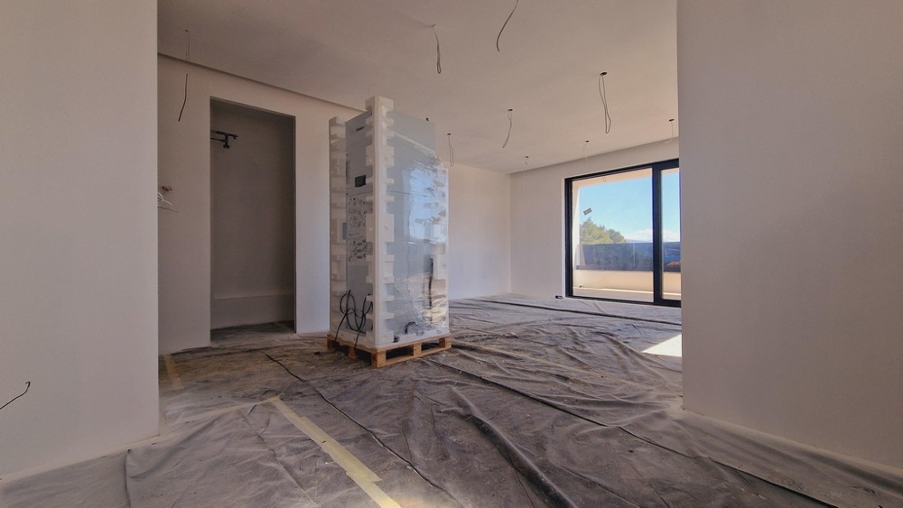Veľký obývací priestor v modernej novostavbe, ktorá je stále vo výstavbe, s oknom a prístupom na terasu.
