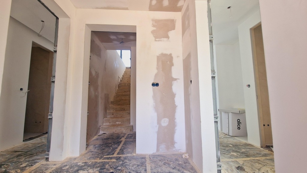 Schodisko a chodba vo výstavbe s viditeľnými škrupinovými stenami a otvorenými káblami.