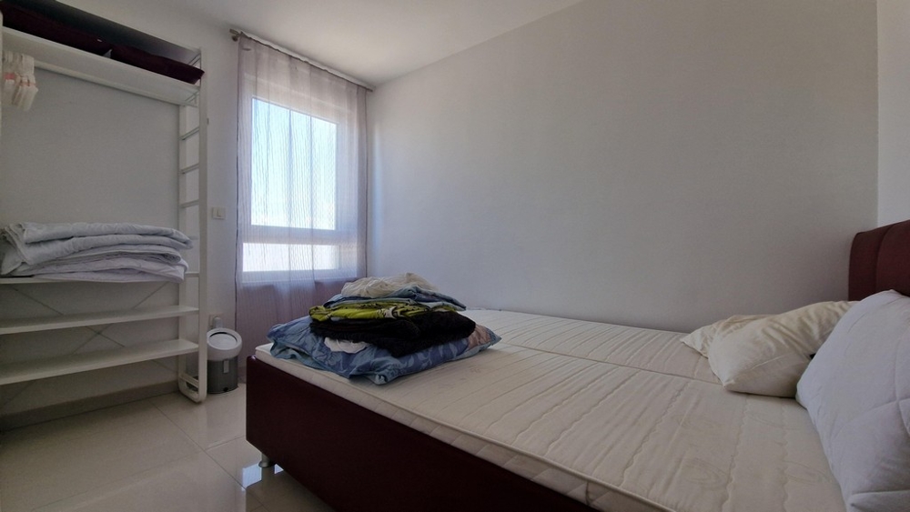 Spálňa s minimalistickým zariadením, oknom a otvoreným úložným priestorom na oblečenie.