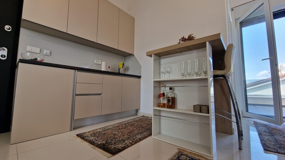 Malá, moderná kuchynka s integrovanými policami a barovými stoličkami, vstup na terasu.