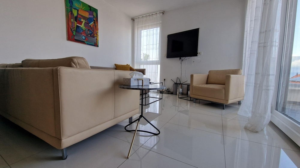 Štýlovo zariadená obývacia izba s pohovkou, TV a veľkými oknami, ktoré prepúšťajú veľa svetla.