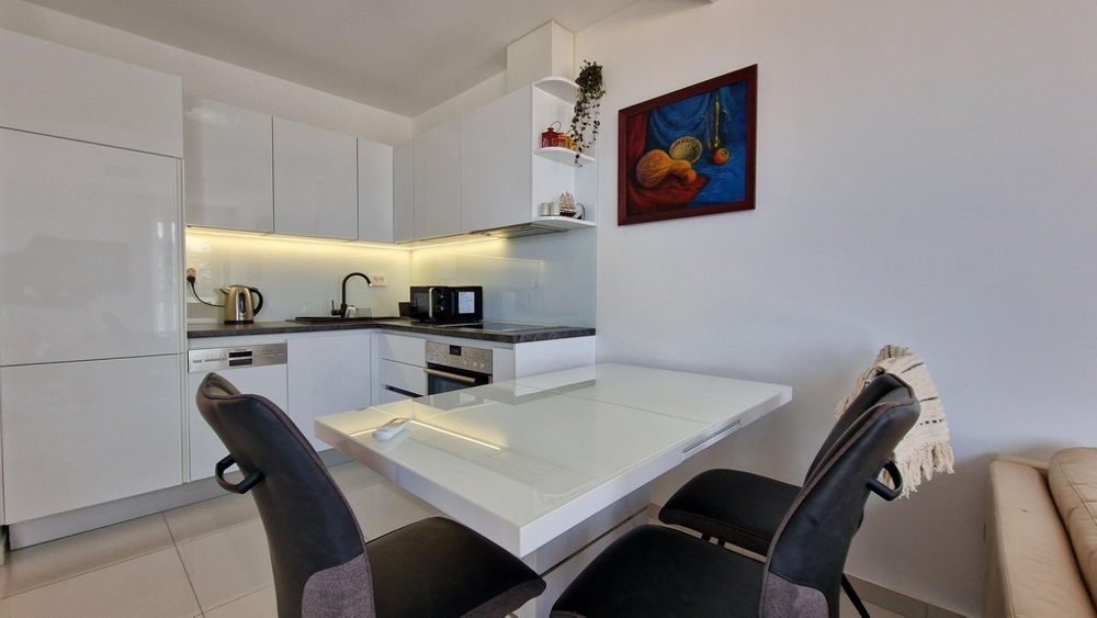 Moderná kuchyňa s bielym vysokolesklým dizajnom, jedálenským kútom a útulným zariadením.