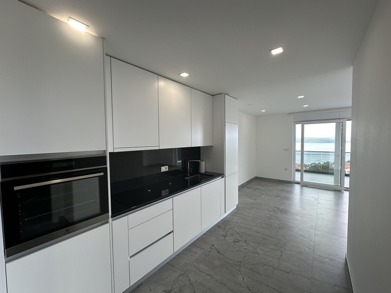 Moderná biela kuchyňa s otvoreným obývacím priestorom a výhľadom na more