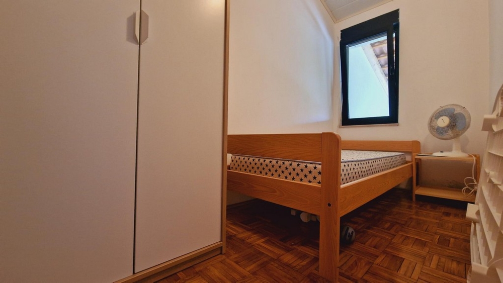 Malá spálňa s posteľou, skriňou a oknom, jednoduché zariadenie.