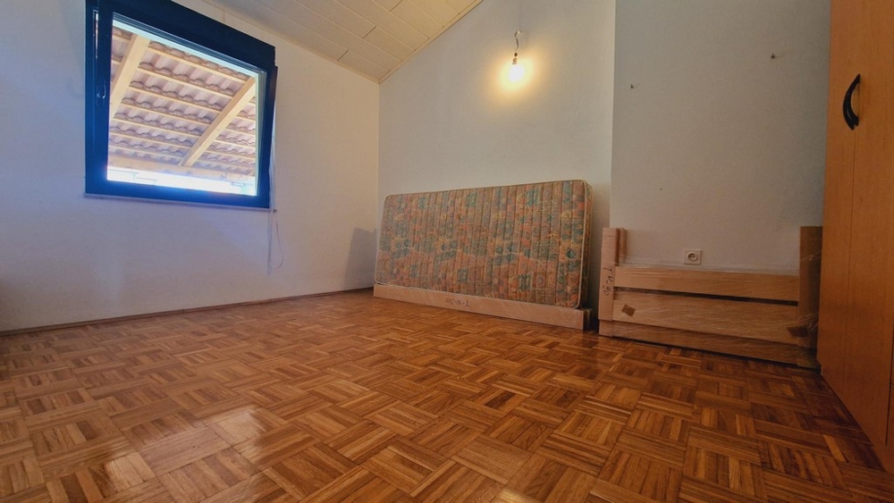 Spálňa s drevenou podlahou a oknom, čiastočne zariadená izba.