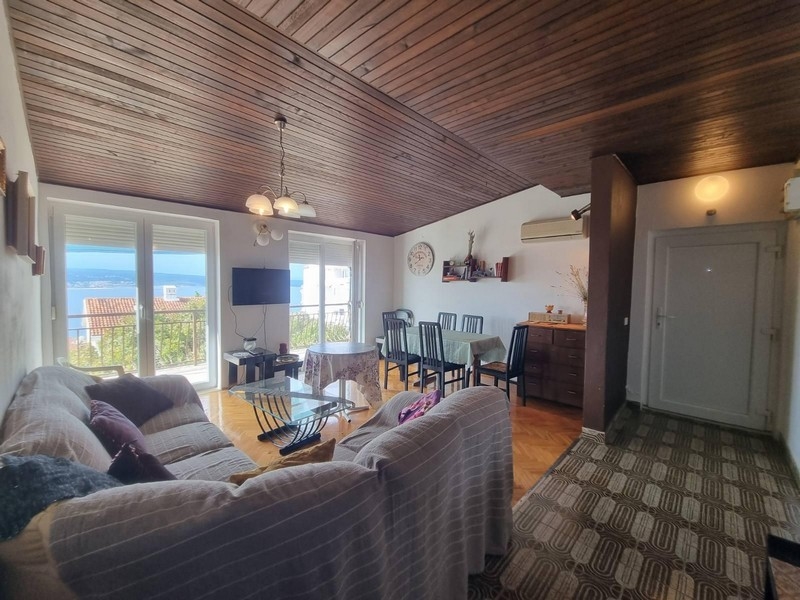 Obývacia izba s prístupom na balkón, dreveným stropom a výhľadom na more.