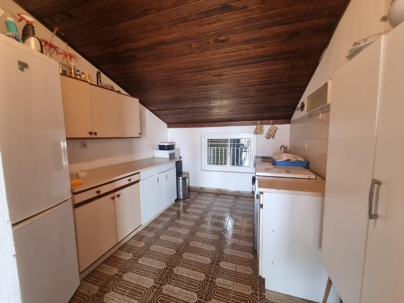 Kuchyňa so šikmým stropom a drevenými trámami, funkčne zariadená.