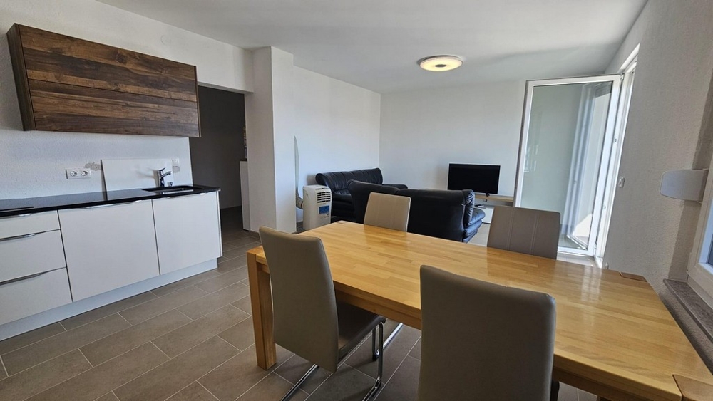 Moderná otvorená kuchyňa s drevenými prvkami, jedálenským kútom a posedením vedúcim na balkón.