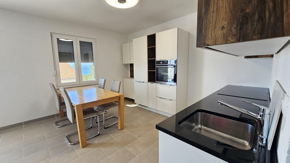 Svetlá kuchyňa s jedálenským stolom, modernými spotrebičmi a oknom s výhľadom na more.