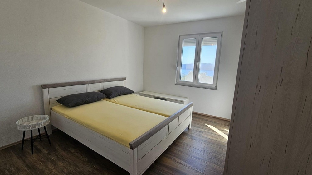 Spálňa s manželskou posteľou a oknom s výhľadom na more.