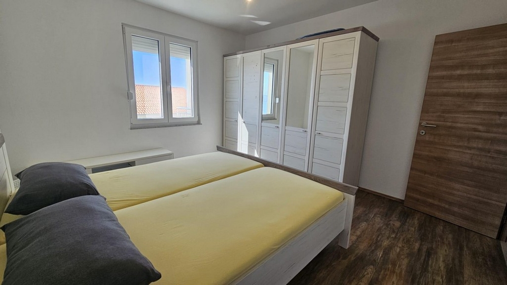 Priestranná spálňa s manželskou posteľou, veľkou skriňou a výhľadom na more cez okno.