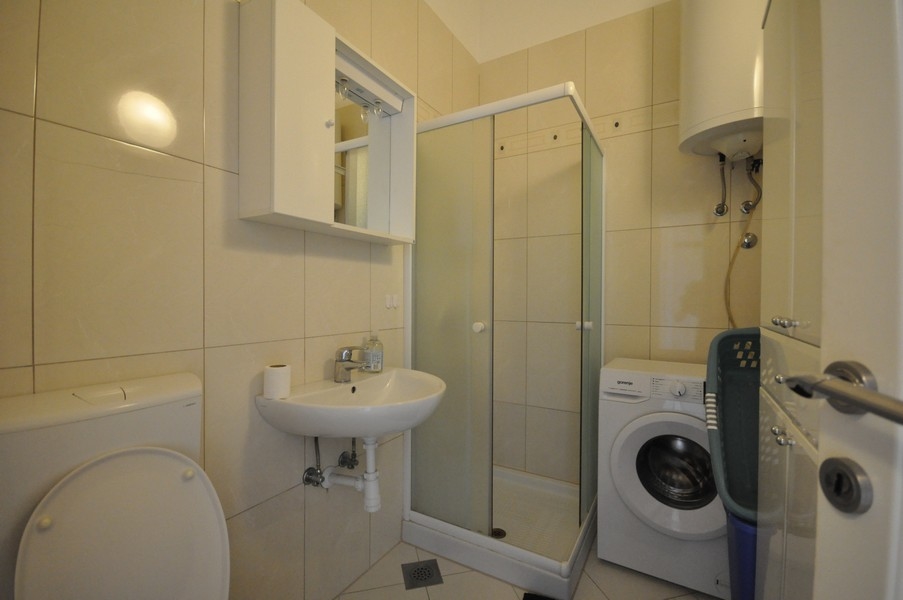 Kúpeľňa so sprchovacím kútom, umývadlom, toaletou a práčkou, steny a podlaha s jasnými dlaždicami