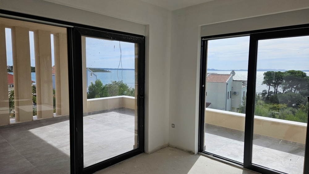 Obývacia izba s veľkými presklenými oknami s výhľadom na more a balkónom