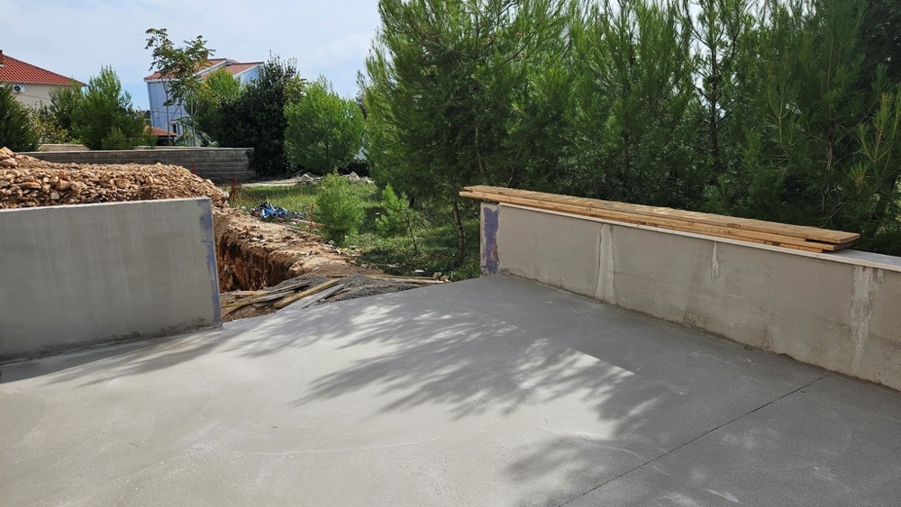 Čiastočne betónová vonkajšia plocha so staveniskami a priekopou pri boroviciach.